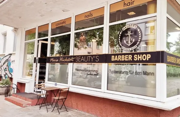 Friseur- und Kosmetiksalon mit Schaufenster, Beschriftung und Außensitzbereich.
