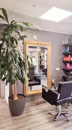 Moderner Friseursalon mit großem Spiegel, Pflanzen und Friseurstuhl im hellen Raum.
